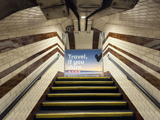 Eine Treppe in einer U-Bahn-Station mit Geländern auf beiden Seiten, die zu einem Schild führt, das oben 'Reise, wenn du wagst' lautet.