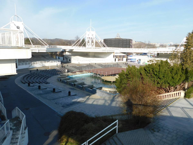 Luftbild des Olympiastadions mit verschiedenen Objekten im Vordergrund und einem bewölkten Himmel im Hintergrund.