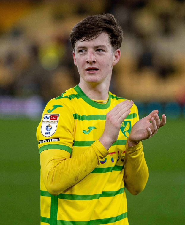 Ein junger Mann in einem gelben und grünen T-Shirt klatscht auf einem Fussballfeld, feiert ein Tor mit einem unscharfen Hintergrund.