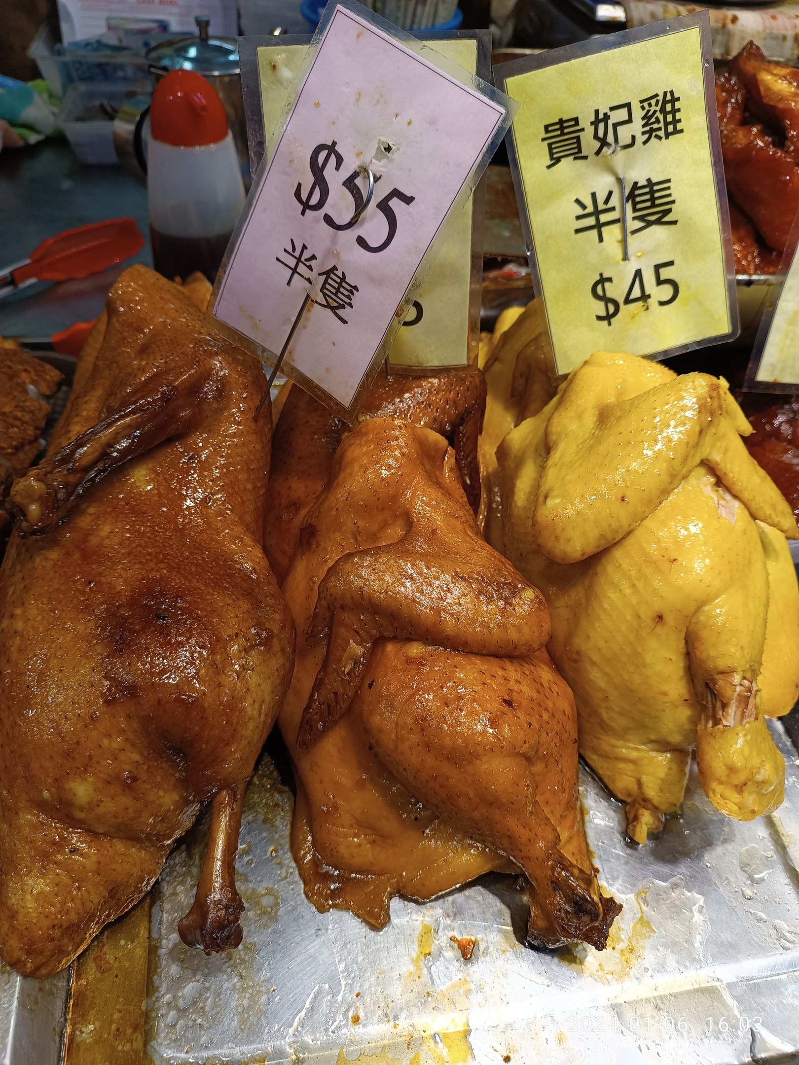 Hühner auf einem Metalltablett mit Preisschildern in einer Marktumgebung.