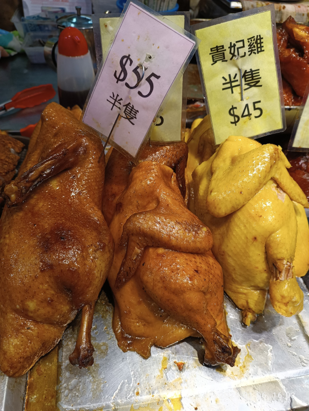 Hühner auf einem Metalltablett mit Preisschildern in einer Marktumgebung.