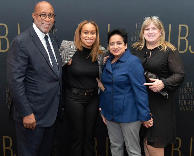 Eine Gruppe von vier Menschen auf einem roten Teppich, die lächeln und für ein Foto posieren, mit einem Schild im Hintergrund, auf dem "Liberty Justice for All Awards" steht.