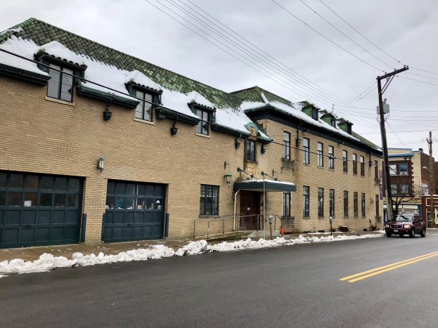 Großes Backsteingebäude mit grüner Dachfläche an einer Straßenkreuzung, umgeben von schneebedeckter Straße, Fahrzeugen, Strommasten mit Kabeln, Bäumen und einem bewölkten Himmel, identifiziert als die ehemalige Feuerwache St. Louis.