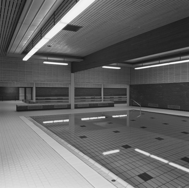 Innenpool mit kristallklarem Wasser, gefliestem Boden, Wänden und Deckenbeleuchtung in einem großen, ruhigen Gebäude.