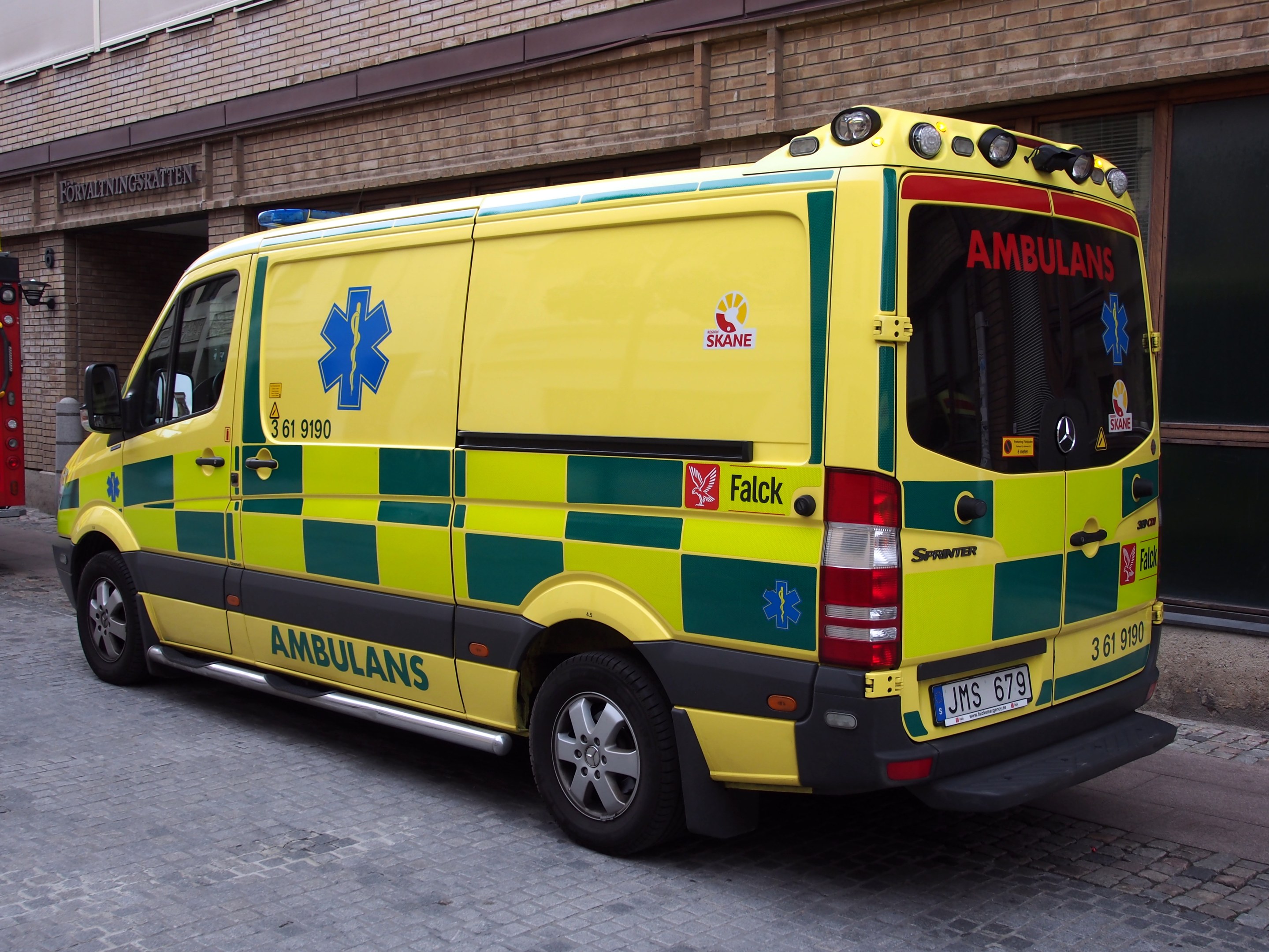Ambulanz auf der Straße vor einem Backsteingebäude mit Text geparkt, mit einem Feuerlöscher auf der linken Seite.
