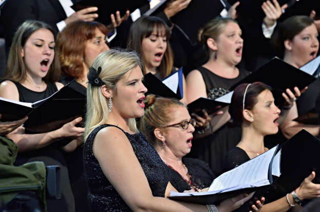 Eine Gruppe von Frauen, die in einem Chor singen, einige halten Bücher, mit einer Person im Vordergrund und einem unscharfen Hintergrund.