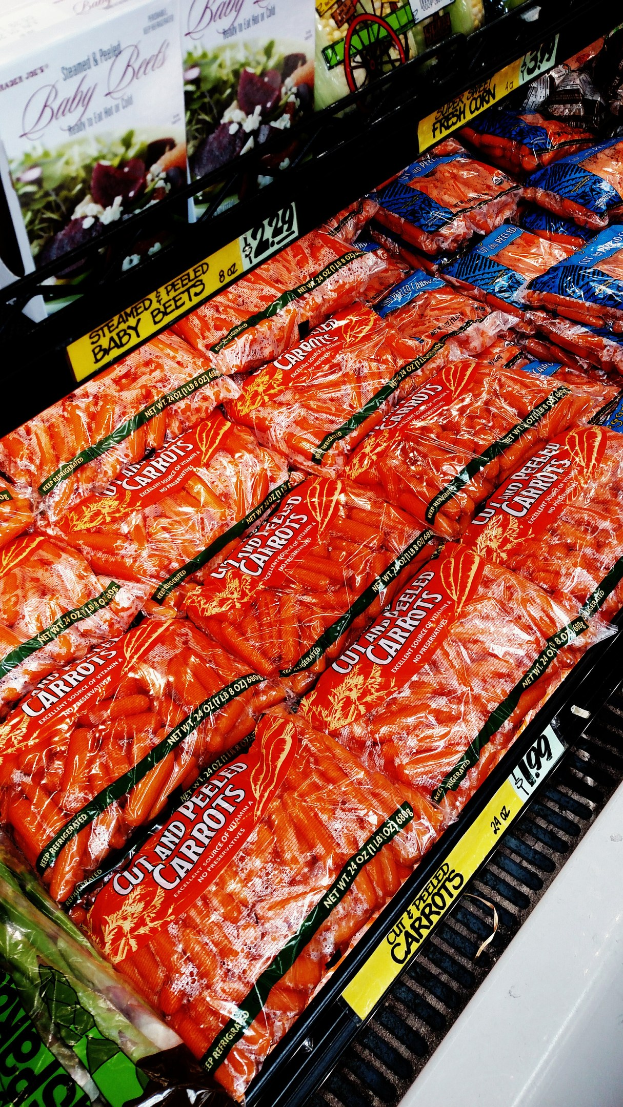 Ein Supermarktregal mit verschiedenen Lebensmitteln, darunter Gemüsepackungen mit angehängten Preisschildern.