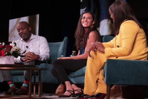 Drei Personen sitzen auf einer Couch vor einem Bildschirm mit einer Vase und einer Flasche auf dem Tisch zwischen ihnen während einer Podiumsdiskussion über Geschlechtergerechtigkeit und Frauenrechte.