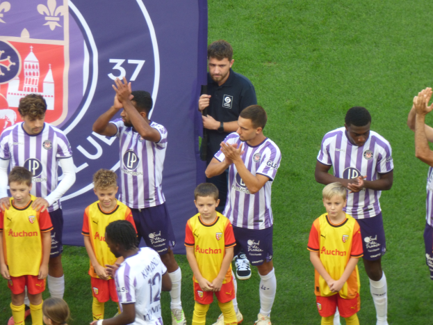 Gruppe junger Jungs auf einem Fußballfeld, die klatschen, mit einem Banner und Logos im Hintergrund.