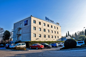 Gebäude mit Fenstern, Treppen und Geländern; ein Schild mit der Aufschrift "ibis budget paris gare de lyon centre"; geparkte Autos, Bäume, Straßenlaternen, Drähte und ein bewölkter Himmel.