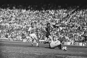 Schwarzes und weißes Foto von Männern, die auf einem Feld Fußball spielen, mit Zuschauern im Hintergrund und einem Banner mit der Aufschrift "Bundesliga 1978-79 Ajax 1-1 Hannover 96".