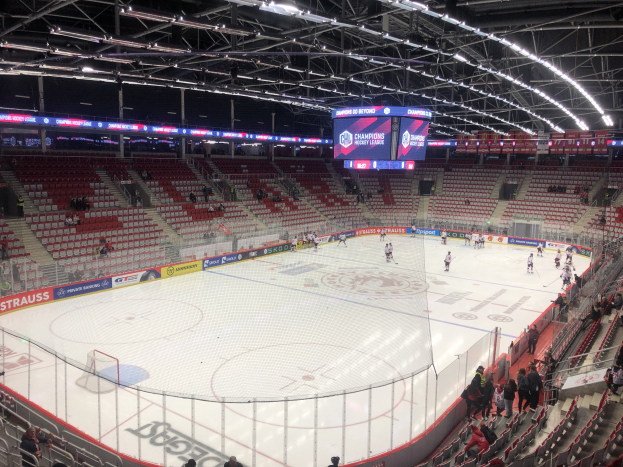 Hockey-Spiel in einer großen Arena zwischen den St. Louis Blues und Detroit Red Wings, mit Zuschauern auf Sitzen und Stehen in der Nähe des Rinks, umgeben von einem Zaun, Anzeigebildschirm, Metallrahmen und Deckenleuchten.