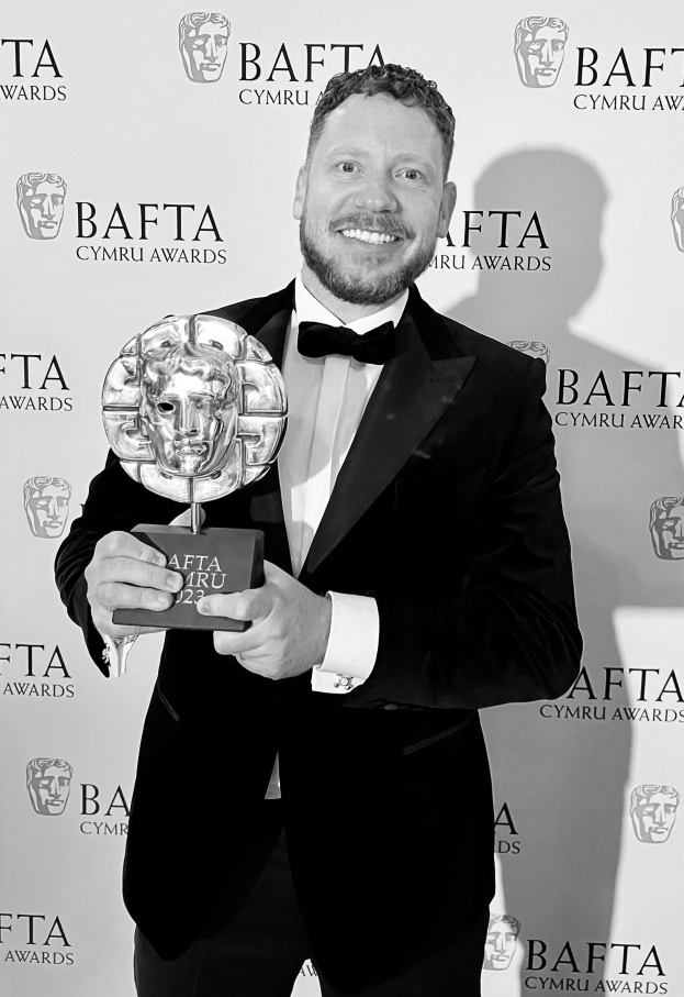 Ein Mann im Smoking hält einen BAFTA-Award und steht vor einem Hintergrund mit der Aufschrift "BAFTA Awards 2018."