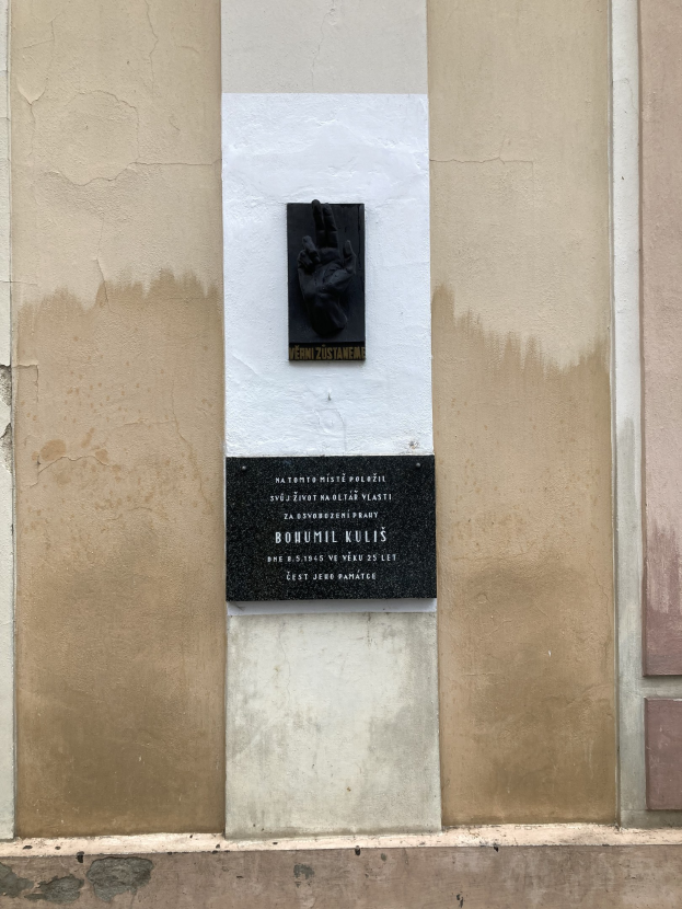 Schwarze Tafel an einem Gebäude mit einer Hand darauf, beschriftet mit Text, wahrscheinlich ein Holocaust-Denkmal.
