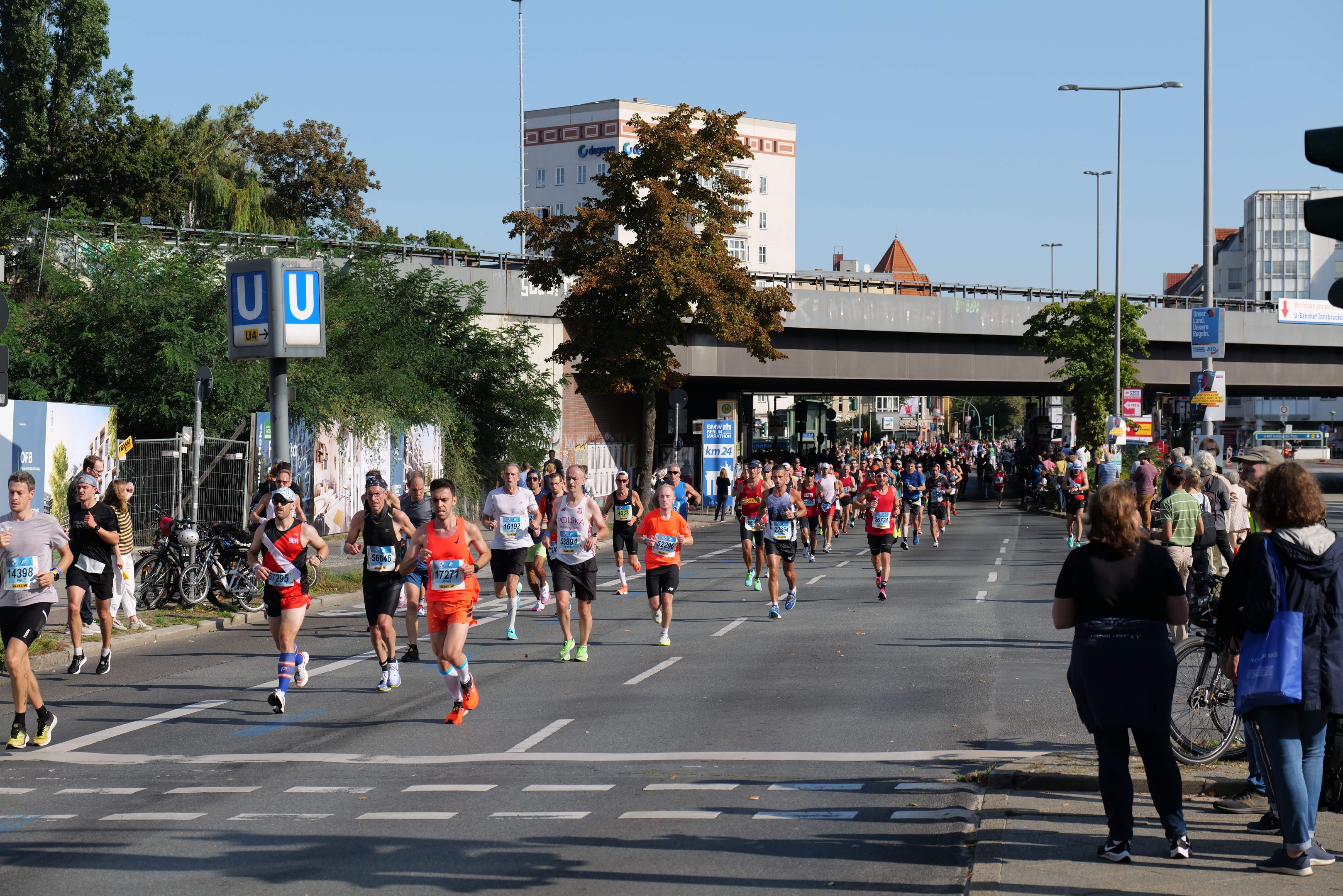 Gruppe von Menschen, die bei einem Marathon auf einer von Bäumen gesäumten Straße unter einem klaren blauen Himmel laufen.