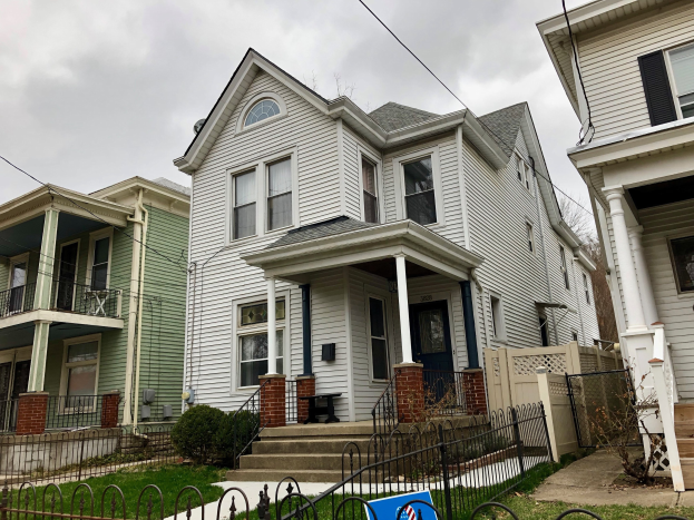 Reihe von Häusern mit Fenstern, Türen, Säulen, Geländern, Stufen und Dächern, umgeben von einem Metallzaun, Gras, Pflanzen, Bäumen und einem bewölkten Himmel, mit einem Mietschild am Boden, das das Objekt unter der Nummer 5901 S Elmwood Ave, Chicago 60618 anbietet.