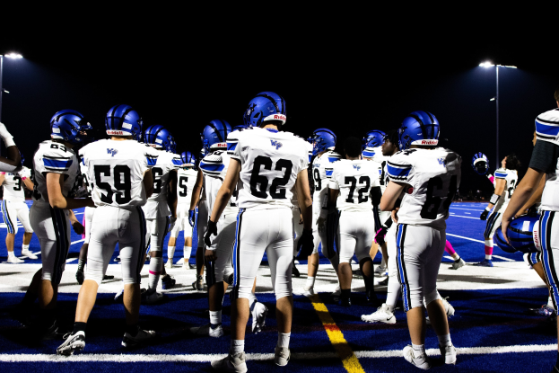 Gruppe von Fußballspielern in Helmen und Stiefeln auf einem Feld unter Flutlicht.