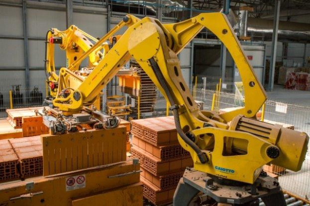 Großes Industriegelände mit gestapelten Kisten, Kränen, Zaun, Polen und einer fernen Wand in einer automatisierten Fertigungsumgebung.