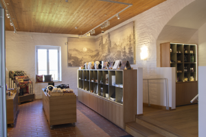 Ein Raum voller verschiedener Einrichtungsgegenstände, darunter ein Tisch mit Gegenständen, Regalen mit Gegenständen, ein Foto auf der Wand, ein Fenster, Deckenleuchten und eine Treppe, Teil eines neuen Ladens in der Altstadt von Heidelberg, Deutschland.