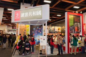 Eine große Gruppe von Menschen an einem Messestand mit Stühlen, Texttafeln, Bannern und Deckenleuchten, die "Book Republic Hong Kong Book Fair" anzeigen.