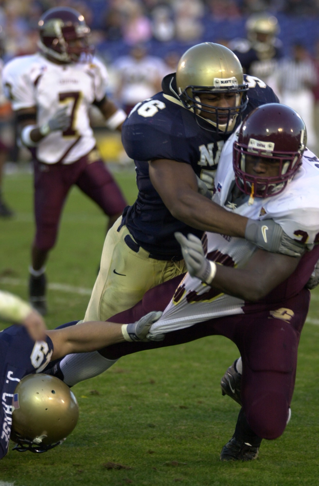Zwei Fußballspieler in Helmen und Uniformen kollidieren auf dem Feld, während andere zuschauen.