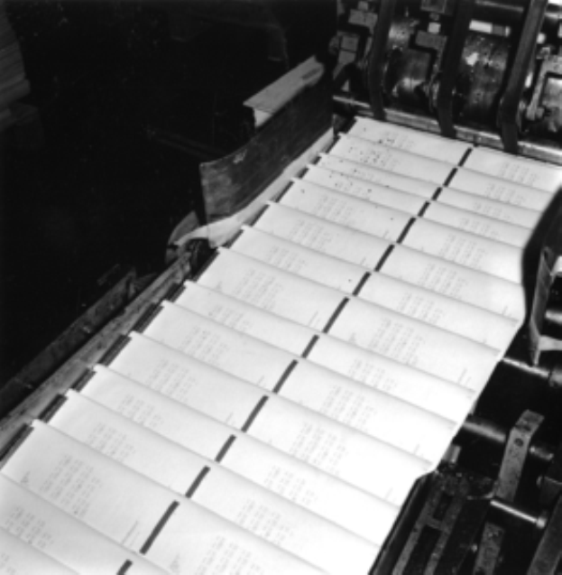 Ein Schwarz-Weiß-Foto einer Druckerpresse mit mehreren Papierbögen darauf.