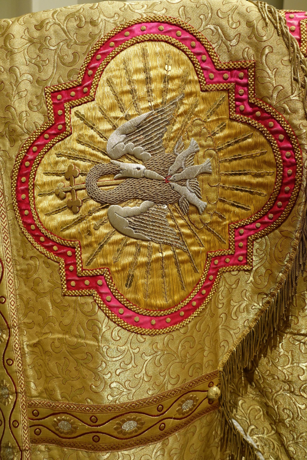 Nahaufnahme eines Priestergewandes mit goldenen und roten Stickereien auf einem Wandhintergrund