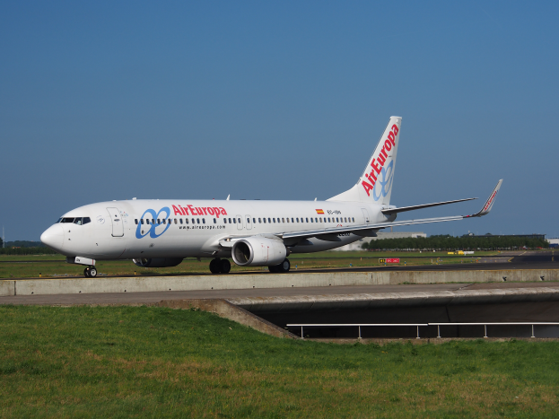 Ein Air Europa Airbus A320-200 auf dem Rollfeld am Frankfurter Flughafen, umgeben von Gras und einem Geländer, mit Bäumen, Gebäuden und einem klaren blauen Himmel im Hintergrund.