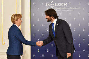 Bundeskanzlerin Angela Merkel und Bundespräsident Joachim Gauck schütteln Hände vor einer Wand mit einem Banner "EU-Gipfel" und einer Tür im Hintergrund, beide lächeln.