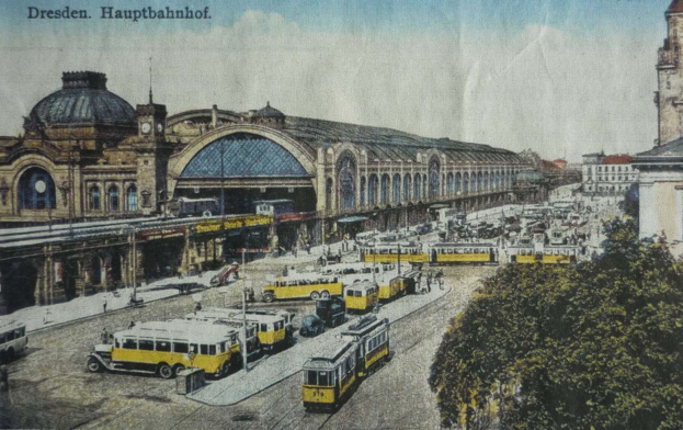 Eine alte Postkarte zeigt den Dresdner Hauptbahnhof in Dresden, Deutschland, mit einer belebten Straßenszene, Fußgängern, Bäumen, Gebäuden und einem bewölkten Himmel.