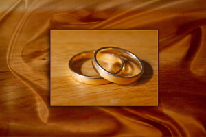 Zwei ineinander verschlungene goldene Eheringe auf einem hölzernen Tisch mit einem goldenen Tuch darüber.