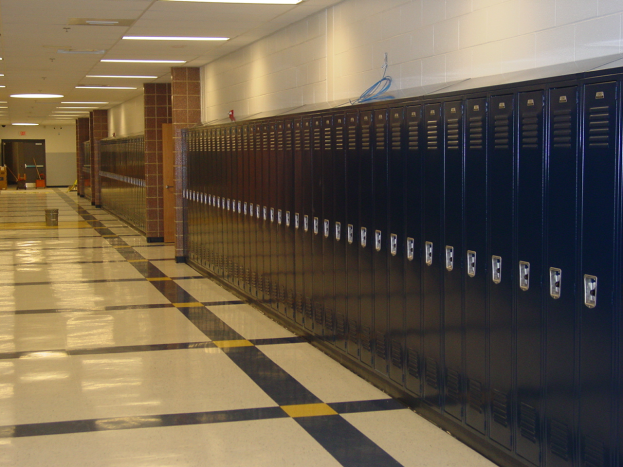 Eine lange Reihe von Spinden in einem Schulflur mit einem gefliesten Boden, einer Wand im Hintergrund, einer Decke mit Lampen und ein paar verstreuten Gegenständen.
