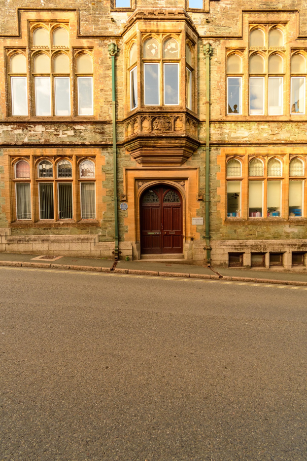 Altes Gebäude mit vielen Fenstern und einer hölzernen Tür an einer Straße, mit Rohren an seinen Wänden.