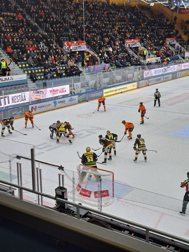 Eine Gruppe von Menschen, die Hockey auf einem Eisstadion spielt, mit Zuschauern im Hintergrund und Beleuchtung von oben.