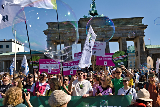 Eine Menschenmenge steht vor dem Brandenburger Tor in Berlin, Deutschland, einige tragen Mützen und Schutzbrillen, halten Fahnen und Schilder und es sind Blasen am Himmel hinter dem historischen Tor und der Statue zu sehen.