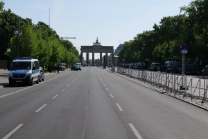 Ein Polizeiwagen steht auf der Seite einer vielbefahrenen Straße vor dem Brandenburger Tor in Berlin, Deutschland, mit Barrieren, Schildern, Bäumen, Laternenpfählen und einer bewölkten Himmel.