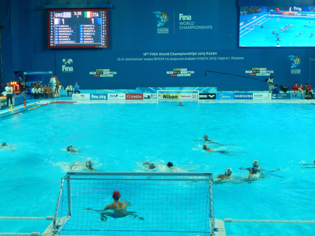 Wasserballspieler bei einem Poolwettkampf während der FINA-Weltmeisterschaften 2016 in Kazan, mit Zuschauern links und einem Hintergrundbild mit Event-Logo.