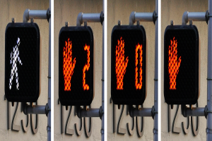 Eine an einem Gebäude angebrachte Ampel, die drei Bilder verschiedener Verkehrssignale zeigt, mit einer Wand im Hintergrund.