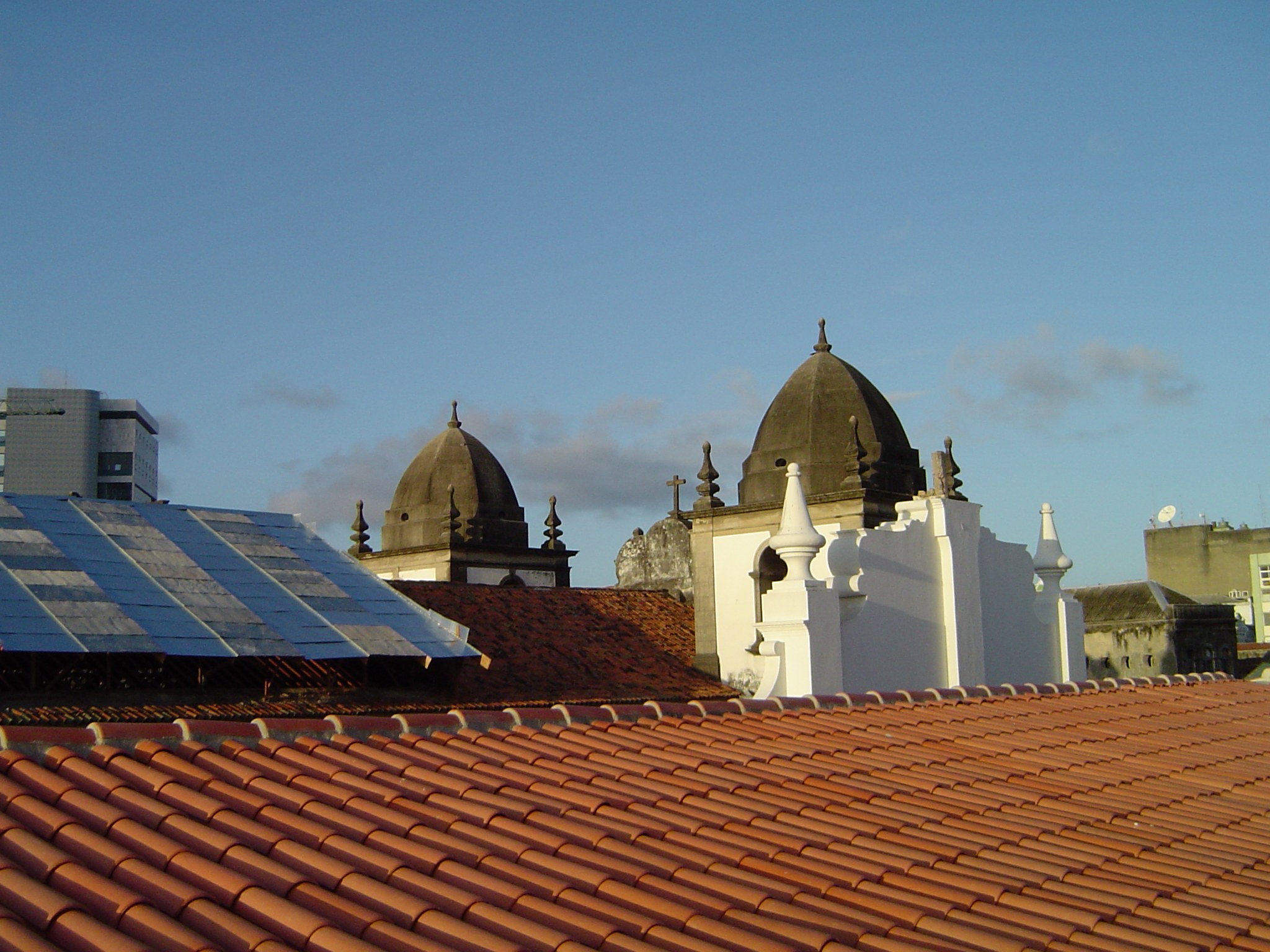Stadtansicht mit mehreren Gebäuden im Vordergrund, einem blauen Himmel im Hintergrund und Solarpanelen auf einem Dach, die den Einsatz von erneuerbarer Energie anzeigen.
