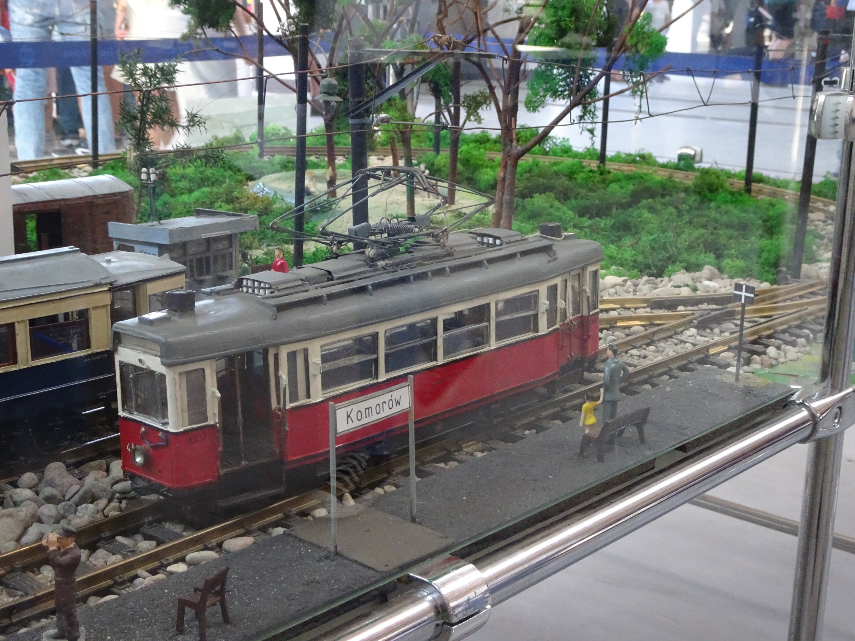 Modellbahn in einer Glasvitrine mit Miniatur-Eisenbahnlandschaft und Zuschauern.