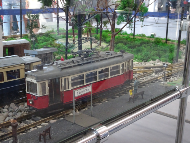 Modellbahn in einer Glasvitrine mit Miniatur-Eisenbahnlandschaft und Zuschauern.