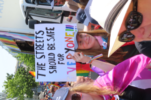 Eine Gruppe von Menschen steht vor einem Lkw und hält ein Schild hoch, auf dem "Die Straßen sollten sicher sein" steht. Einige tragen Mützen und Schutzbrillen, andere halten Schilder, vor einem Hintergrund aus Bäumen, Gebäuden und einem klaren blauen Himmel.