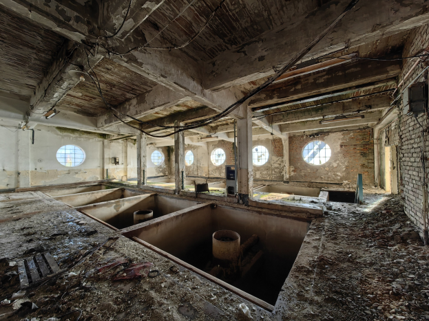 Verlassenes Gebäudeinnere im Chernobyl-Ausschlussgebiet, das verstreute Trümmer, freiliegende Wände, Decke und bauliche Elemente wie Säulen und Rohre zeigt.