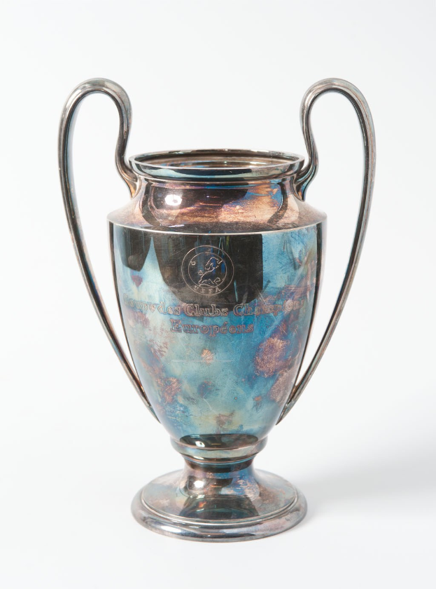 Der UEFA Champions League Pokal, ein stahlerner Becher mit zwei Handles, blau und silbern in der Farbe, mit der Aufschrift "UEFA Champions League", dargestellt vor einem weißen Hintergrund.