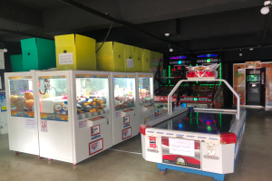 Ein Raum voller verschiedener Arcade-Spiele, mit einem Spielautomaten auf der rechten Seite, einem Boden unten und einer Decke mit Lichtern oben.