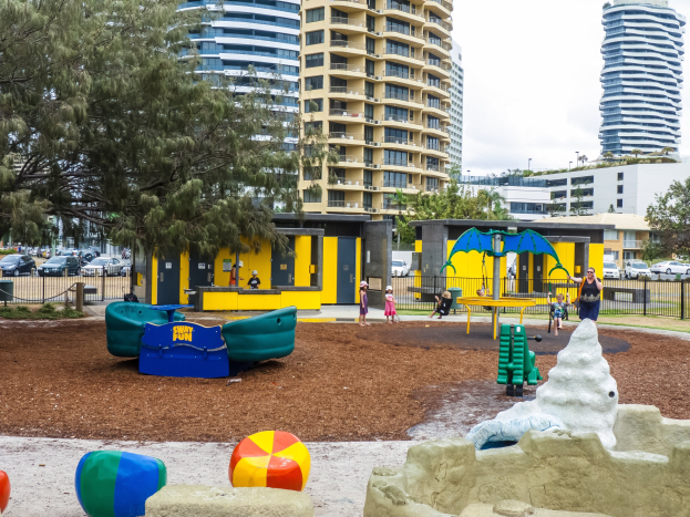 Spielplatz mit Kindern auf Geräten, umgeben von Bäumen und hohen Gebäuden in einer städtischen Umgebung.