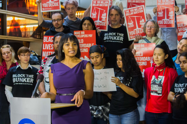 Eine Aktivistin von Black Lives Matter spricht in ein Mikrofon an einem Rednerpult, während sie eine Menge anspricht, die Schilder hält.