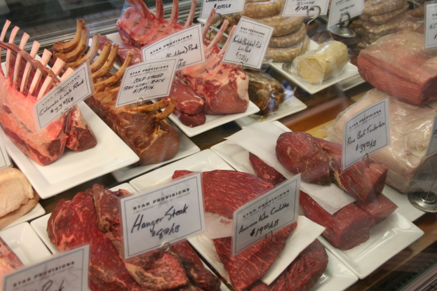 Vitrine in einer Metzgerei mit verschiedenen Fleischsorten auf weißen Tellern, jeweils mit Preisschild beschriftet.