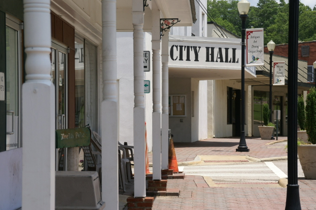Rathaus mit umliegenden Gebäuden, Straßeninfrastruktur, Fahrzeugen, Verkehrsmanagement-Artikel und Grünflächen unter einem bewölkten Himmel.