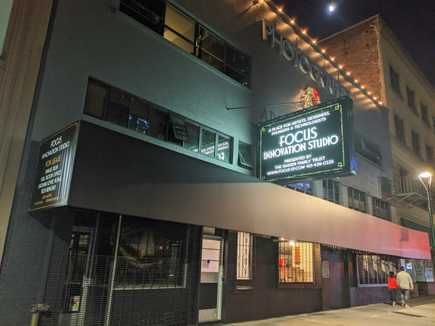 Das Focus Innovation Studio in New York City bei Nacht, mit beleuchteten Fenstern und Namensschildern an umliegenden Gebäuden, Menschen auf dem Gehweg und dem Himmel im Hintergrund.